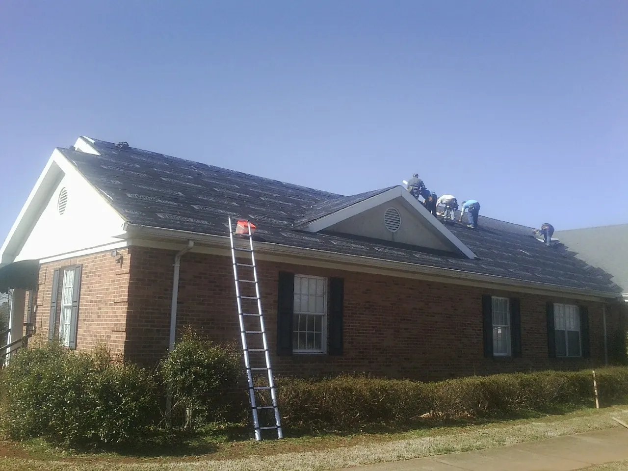 Crew tearing shingles off a brick ranch roof with a ladder set — Metal Roof Repair work by our crew in Rufus