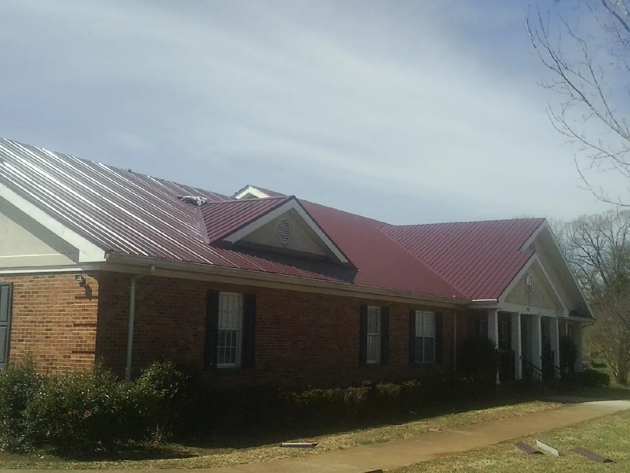 Red metal roof with gabled entries on a long brick building, from a Hail Damage Roof Repair job in Rufus