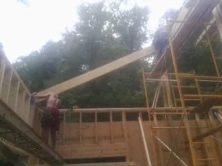 Carpenter raising a rafter beam on a new second story frame in Rufus