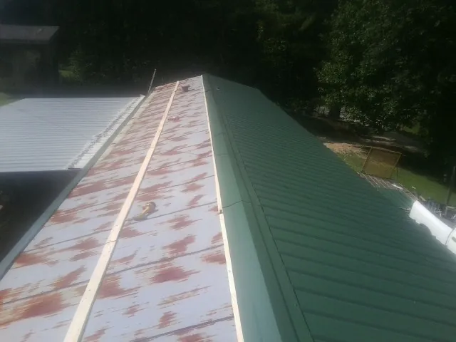 Old rusted panels beside newly installed green metal roofing — Wind Damage Roof Repair by Roofing Brothers in Rufus