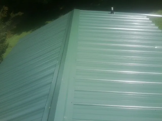 New green metal panels meeting at the ridge of a roof — Flat Roof Repair work by our crew in Rufus