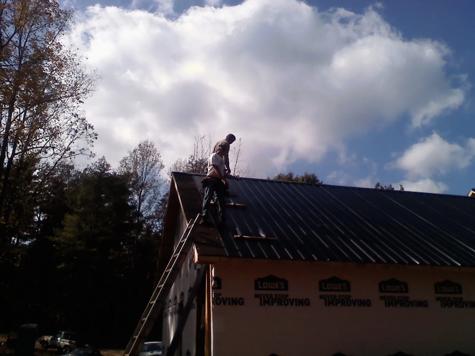 Roofer fastening dark metal panels high against a cloudy sky, from a Roof Inspection job in Rufus