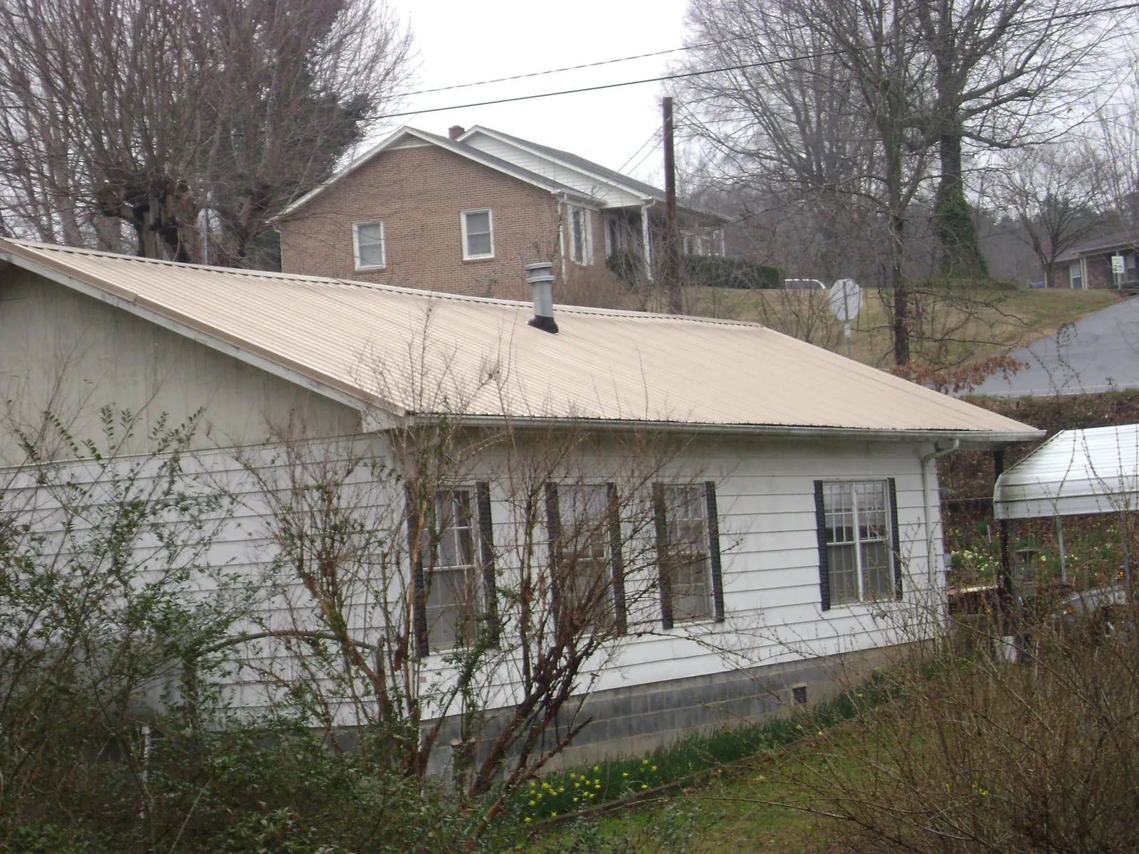 Tan metal roof on a white sided house set into a hillside — Commercial Roofing by Roofing Brothers in Rufus