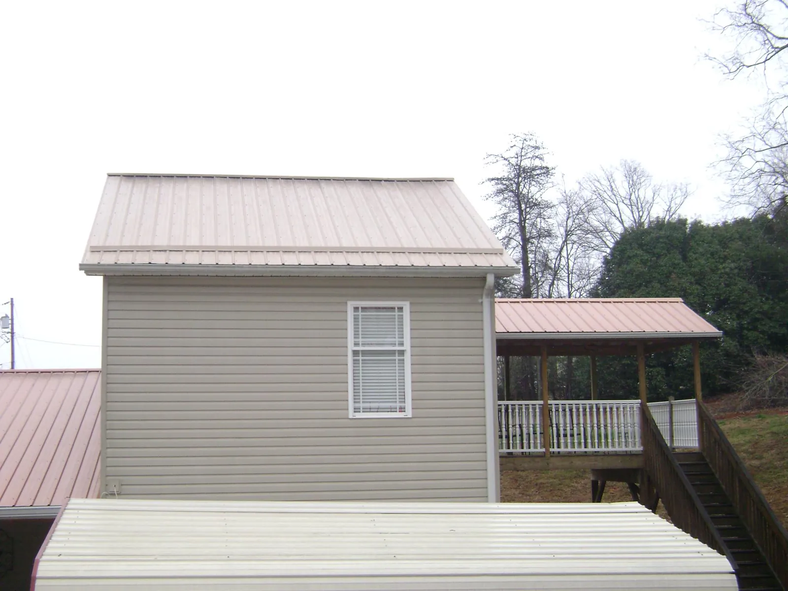 Tan metal roofs on a two story addition and attached porch, from a Roof Replacement job in Rufus
